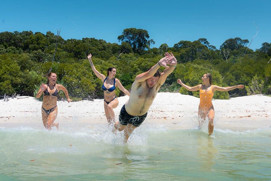 Friends in swimwear running and jumping into the sea on the beach
