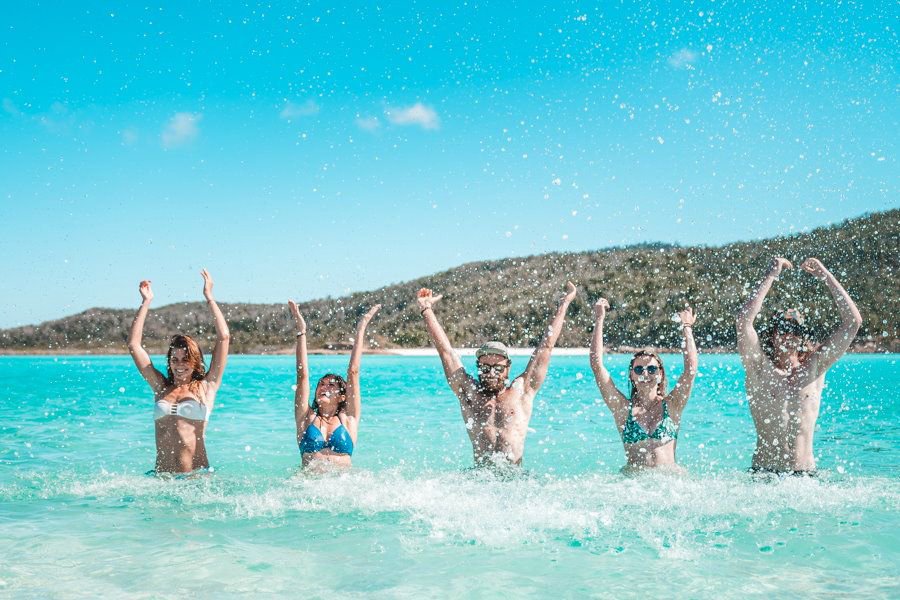 Group of friends jumping and splashing in clear turquoise water at a tropical Whitsundays beach