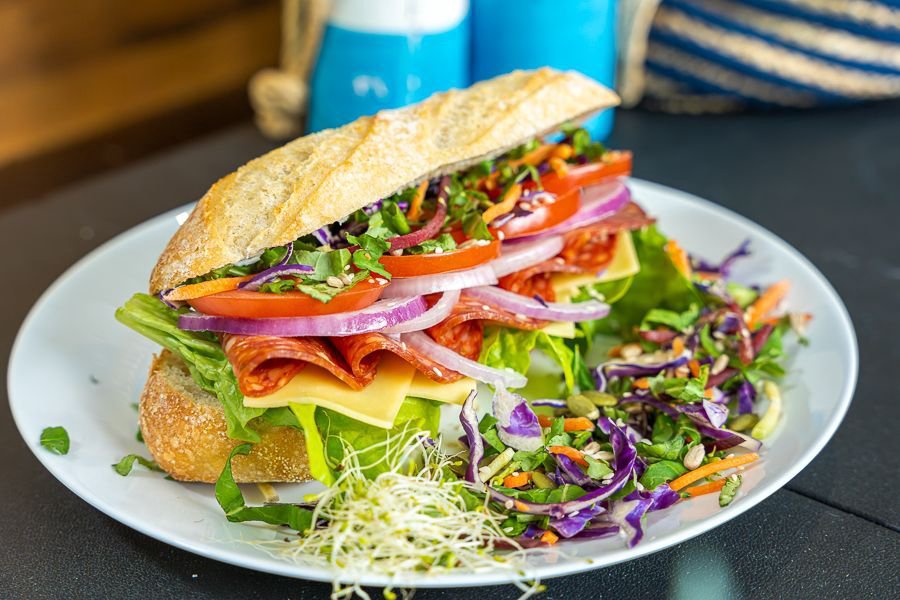 Fresh gourmet deli sandwich with salami, cheese, tomato, red onion and leafy greens served with a side salad