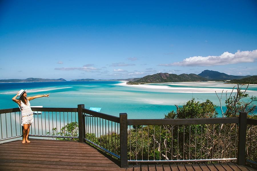 Woman standing on a timber lookout platform overlooking the swirling white sands and turquoise waters of Hill Inlet in the Whitsundays.
