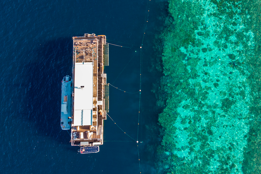 Top-down aerial view of a reef pontoon floating beside vibrant turquoise coral reef waters in the Whitsundays