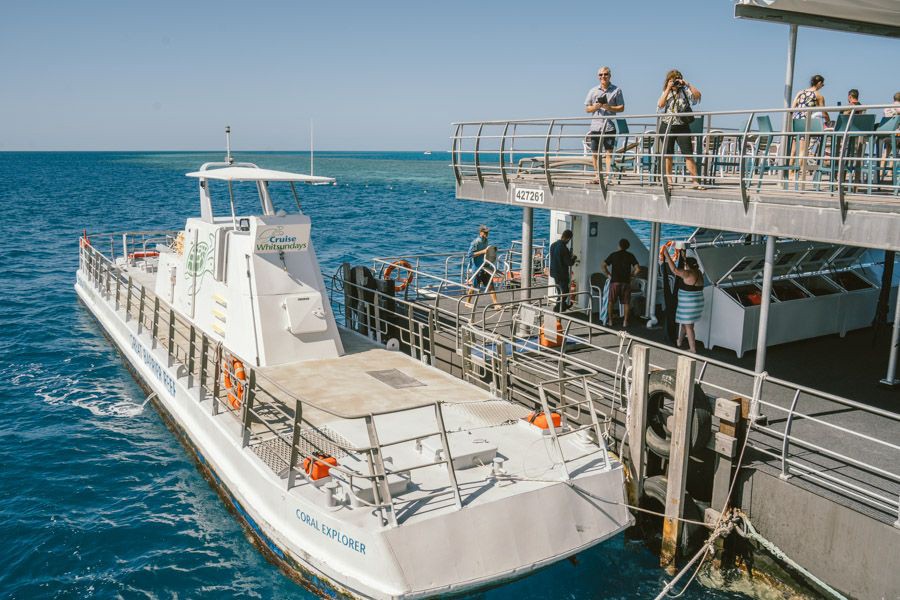 Cruise Whitsundays Coral Explorer vessel moored beside the Reefworld pontoon with guests standing on the upper deck overlooking the ocean