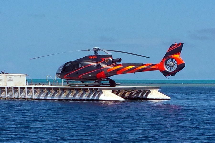 Black and red helicopter parked on a floating reef pontoon surrounded by blue ocean in the Whitsundays