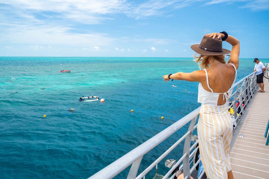 Woman in a sunhat standing on a reef pontoon walkway overlooking turquoise water and snorkellers in the Whitsundays