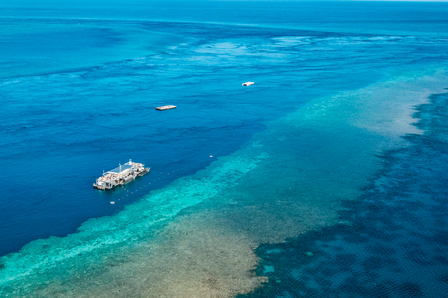 Aerial view of Reefworld pontoon anchored on the edge of the Great Barrier Reef, surrounded by deep blue ocean and turquoise coral formations