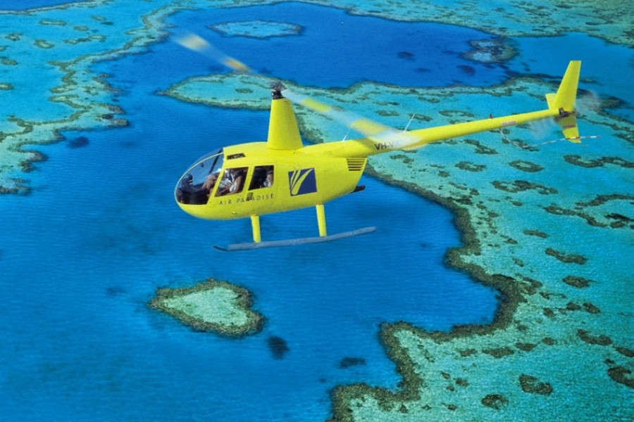 Bright yellow helicopter flying over the turquoise waters and coral formations of Heart Reef in the Great Barrier Reef