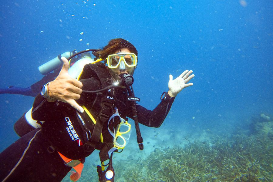 Scuba diver underwater giving a shaka hand sign while exploring the coral reef in clear blue water
