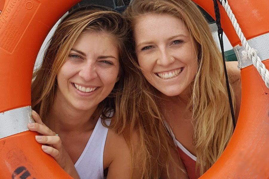 Two smiling women pose together through an orange life ring on a boat, enjoying a sunny day out on the water in the Whitsundays