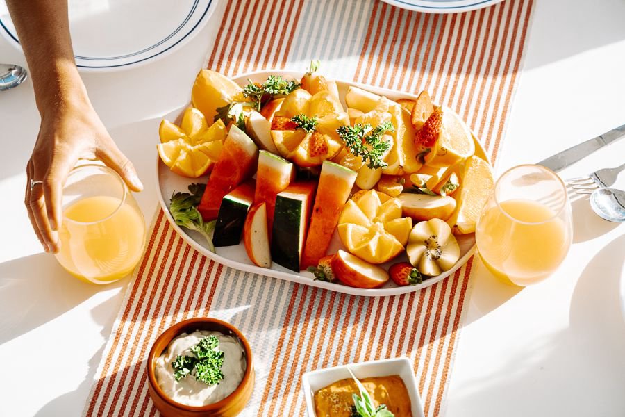 Overhead view of a tropical fruit platter with watermelon, apple, citrus and strawberries served with glasses of juice
