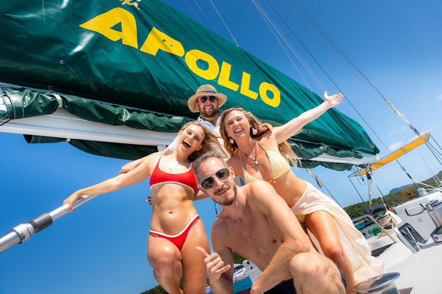 Group of young friends smiling and posing on the deck of the sailing boat Apollo under bright blue skies in the Whitsundays