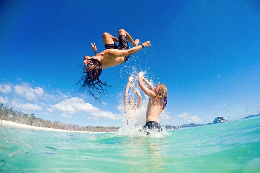 Group of friends laughing and doing a backflip into shallow turquoise water in the Whitsundays on a sunny day