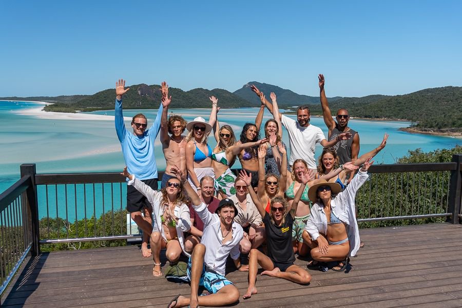 Large group of friends posing with arms raised at Hill Inlet lookout overlooking Whitehaven Beach and turquoise waters in the Whitsundays