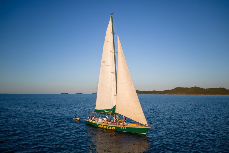 Maxi Apollo sailing yacht with full white sails cruising on calm ocean waters at sunset in the Whitsundays