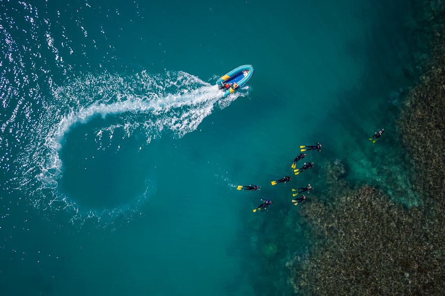Aerial view of snorkellers exploring a coral reef while a small tender boat circles nearby in clear turquoise waters of the Whitsundays