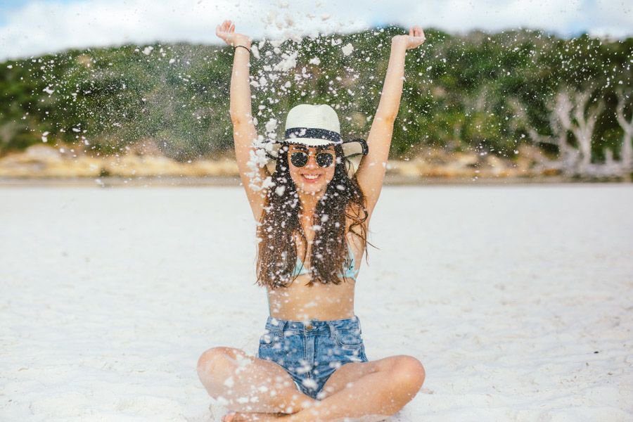 Guest sitting on Whitehaven Beach throwing sand in the air during a Whitsundays visit