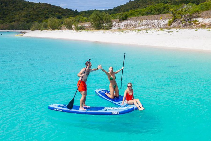 Guests stand up paddleboarding in clear turquoise waters near a Whitsundays beach