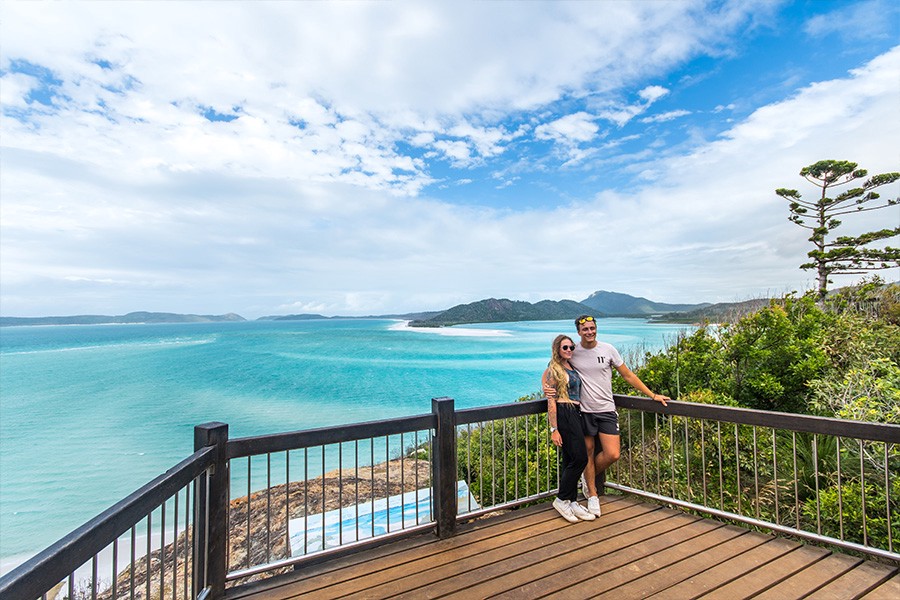 Couple standing at Hill Inlet lookout overlooking the swirling white sands and turquoise waters of Whitehaven Beach in the Whitsunday Islands, Queensland.