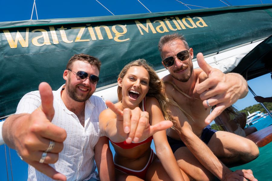 Group of friends smiling and making shaka hand signs onboard the Waltzing Matilda sailing boat in the Whitsundays, Queensland