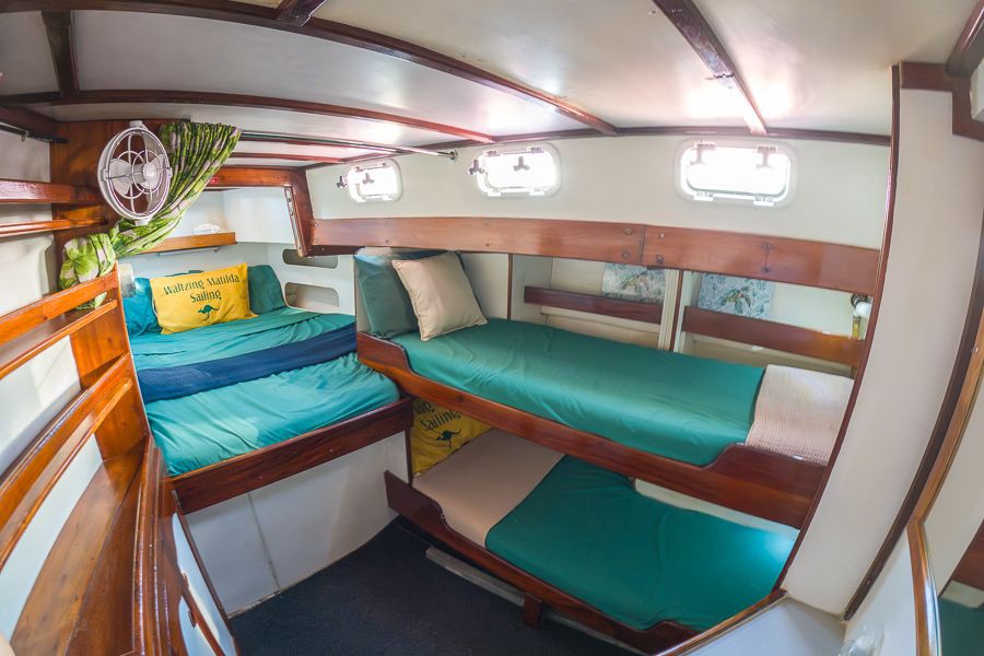 Comfortable bunk cabin inside the Waltzing Matilda sailboat featuring timber finishes, green bedding and porthole windows in the Whitsundays.