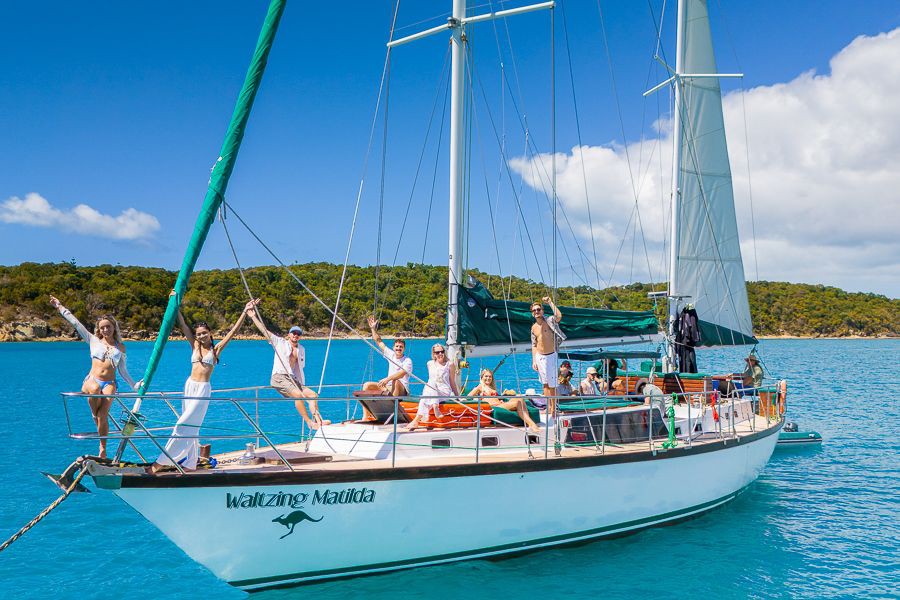 Guests enjoying the sun on board the Waltzing Matilda sailboat surrounded by turquoise water in the Whitsunday Islands, Queensland, Australia.