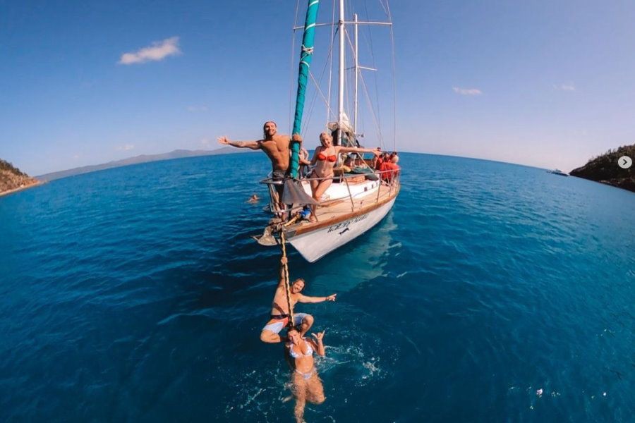 Guests jumping and swimming beside the Waltzing Matilda sailing yacht in the turquoise waters of the Whitsundays, Queensland