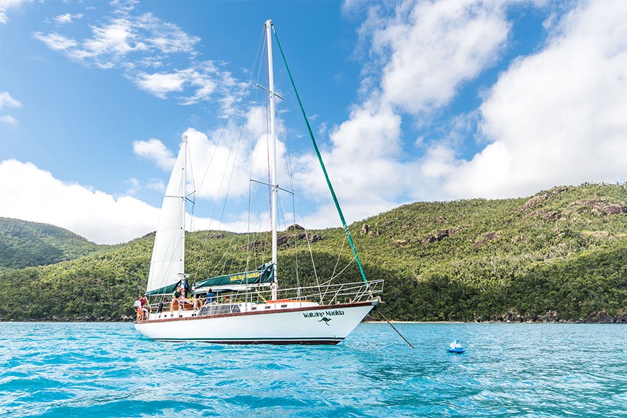 Waltzing Matilda sailing yacht anchored in turquoise waters off the Whitsunday Islands with lush green hills in the background