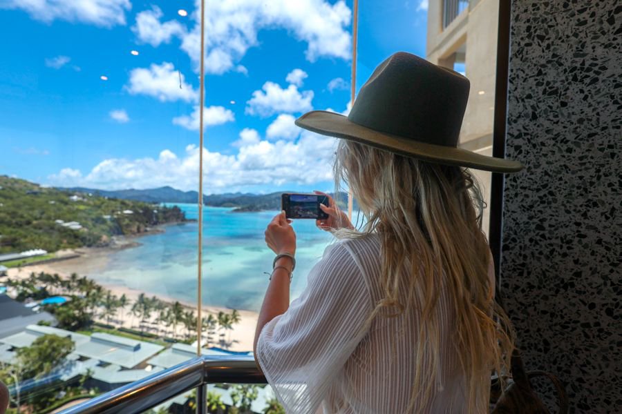 Woman taking a photo of the Airlie Beach coastline and turquoise waters from a balcony viewpoint