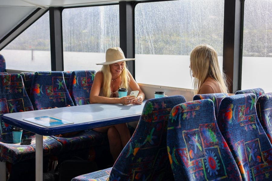 Two women enjoying coffee inside a ferry cabin while travelling through the Whitsundays