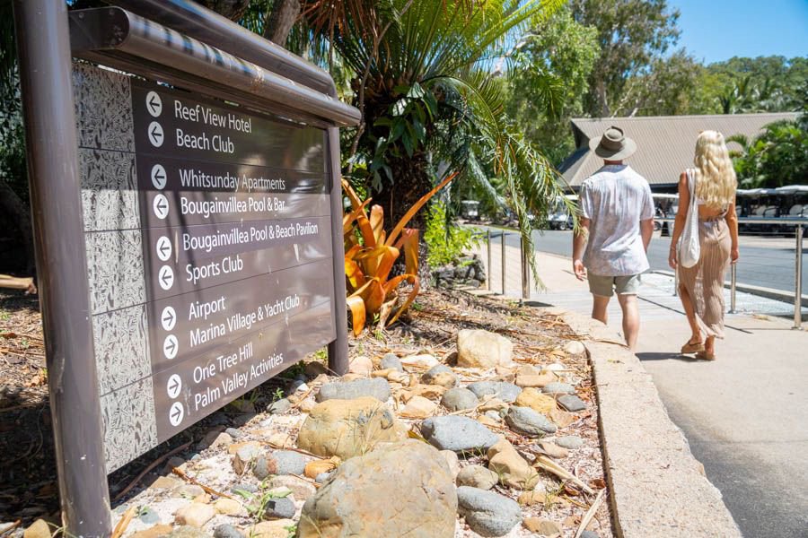 Couple walking past a directional sign on Hamilton Island pointing to hotels marina and island attractions