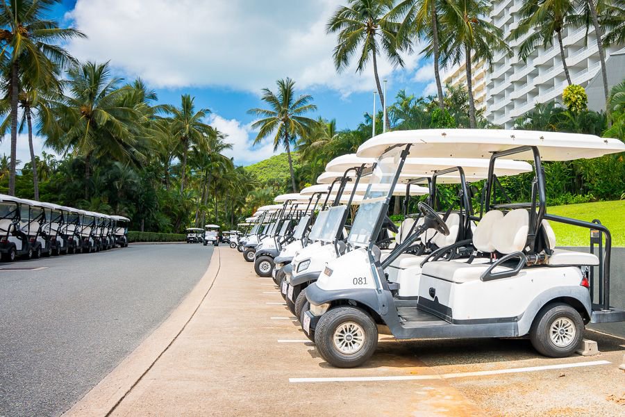 Row of white golf buggies parked along a palm-lined road at Hamilton Island resort