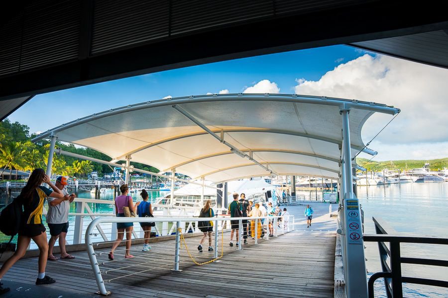 Visitors walking down a covered marina gangway to board boats at Airlie Beach