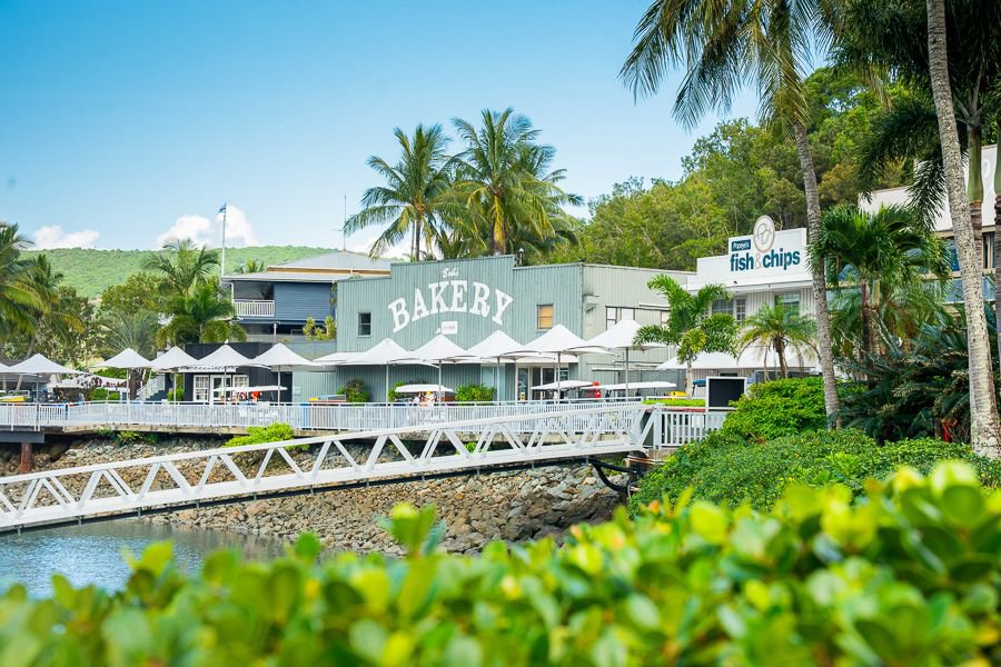 Waterfront boardwalk at Hamilton Island Marina Village with bakery and fish and chips shops surrounded by palm trees