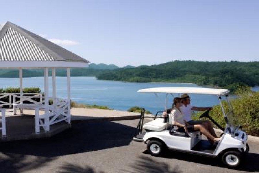 Couple driving a golf buggy along a coastal road on Hamilton Island with ocean views and a white gazebo in the foreground