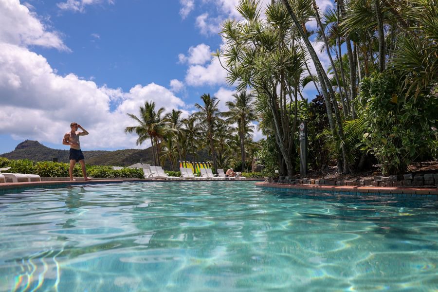 Man standing beside a tropical resort pool surrounded by palm trees on Hamilton Island