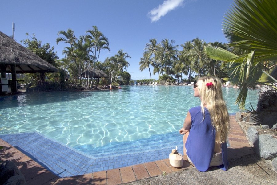 Woman sitting beside a tropical lagoon-style pool surrounded by palm trees in the Whitsundays