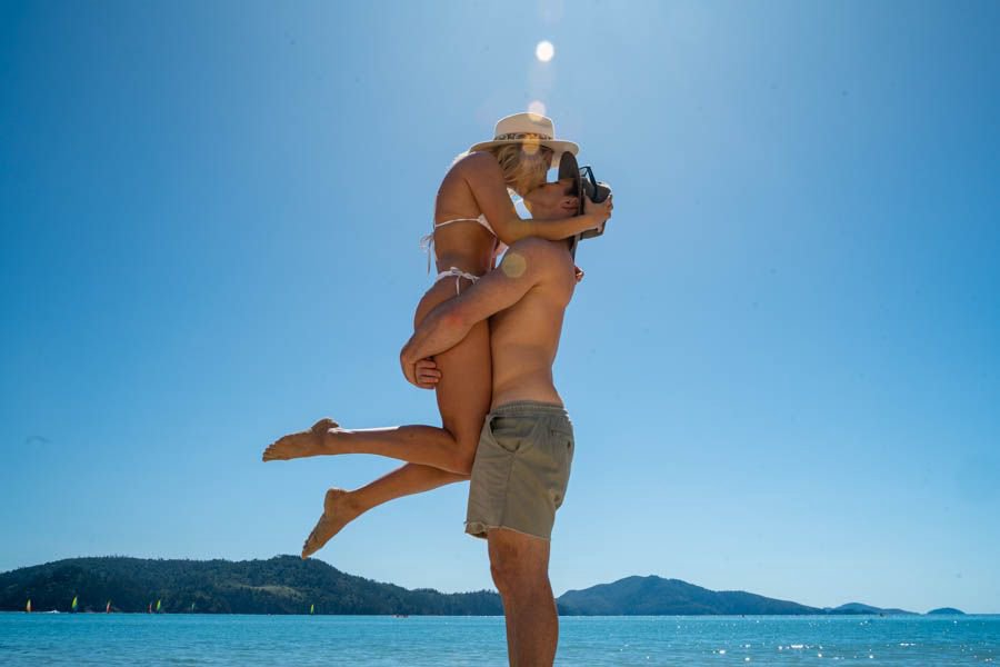 Couple embracing on a sunny beach with turquoise ocean and island backdrop in the Whitsundays