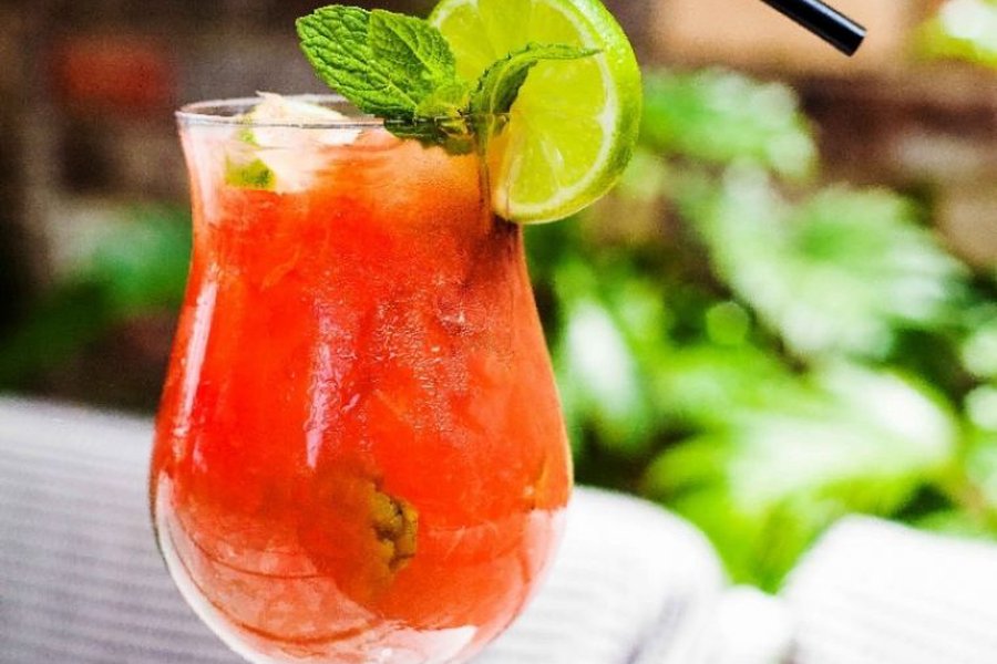 Close up of a red watermelon cocktail garnished with fresh mint leaves and a lime slice in a stemmed glass