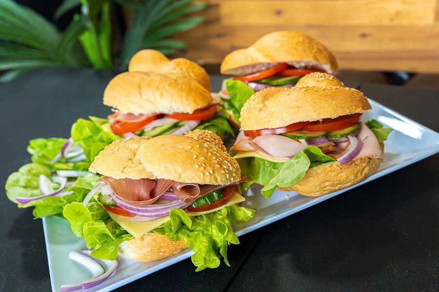A platter of freshly made gourmet sandwiches with ham, cheese, lettuce, tomato, and red onion served on soft rolls