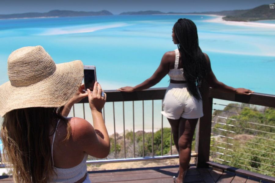 Two women at Hill Inlet Lookout, one taking a photo while the other overlooks the swirling white sands and turquoise waters of Whitehaven Beach