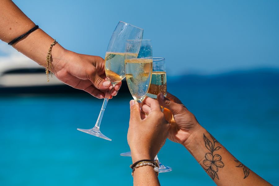 Three friends clinking champagne glasses together against the backdrop of turquoise Whitsundays waters on a sunny day