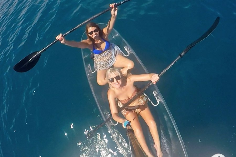 wo women paddling a transparent kayak over deep blue ocean water on a sunny day