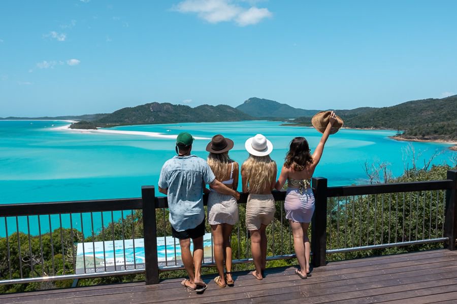 Four friends standing at a lookout railing, gazing out over the swirling white sands and turquoise waters of Hill Inlet in the Whitsundays