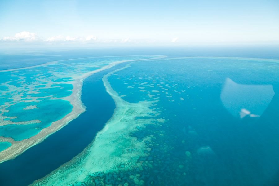 Panoramic aerial view of turquoise reef formations and deep blue channels in the Great Barrier Reef.