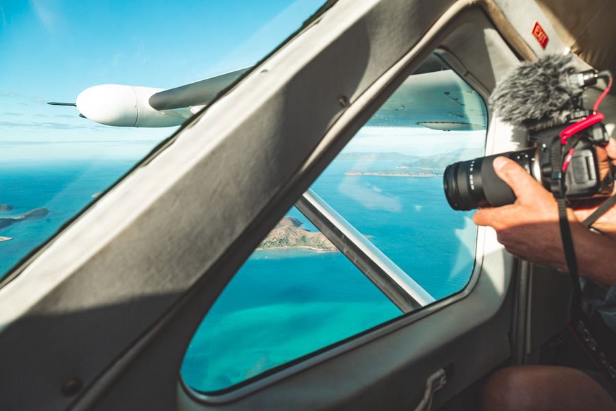 Passenger photographing the turquoise Whitsundays coastline through a small aircraft window during a scenic flight.