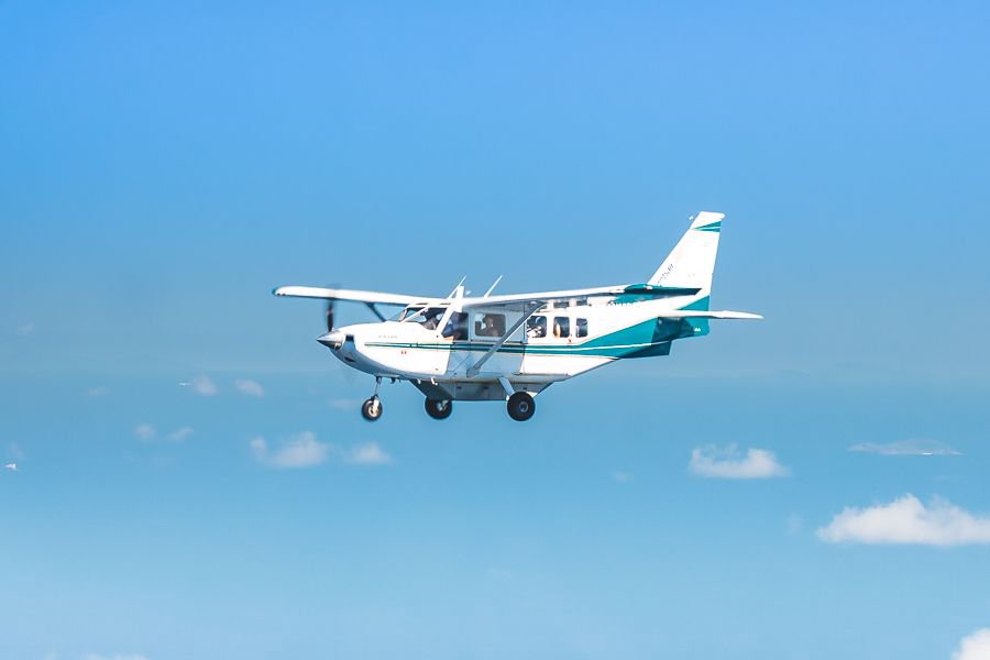 Small white and teal Whitsundays plane flying against a clear blue sky during a scenic reef and island flight.