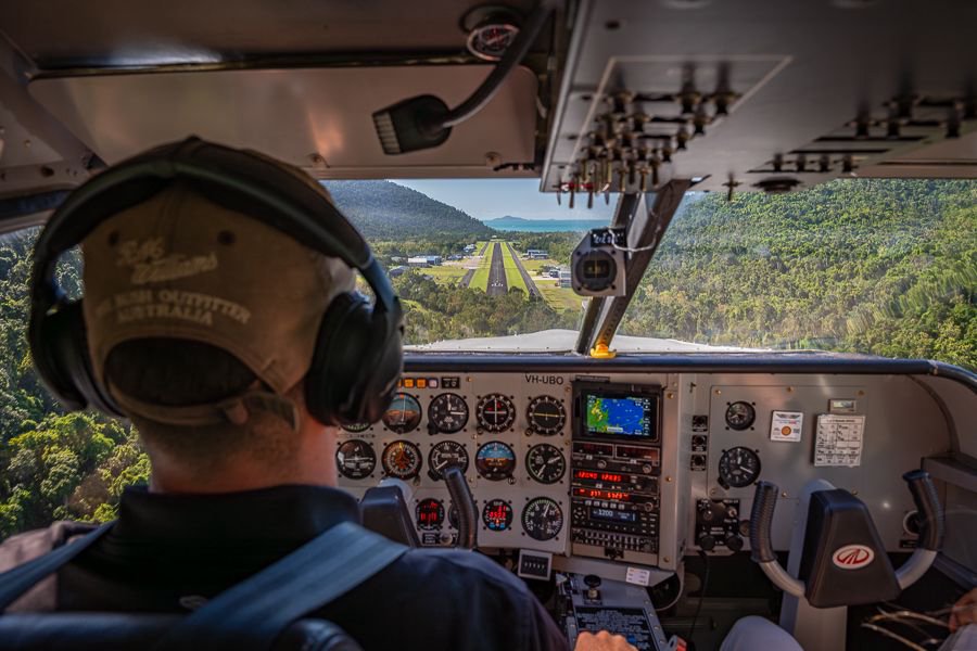 View from inside a small aircraft cockpit as the pilot approaches a tropical runway surrounded by lush green hills in the Whitsundays.