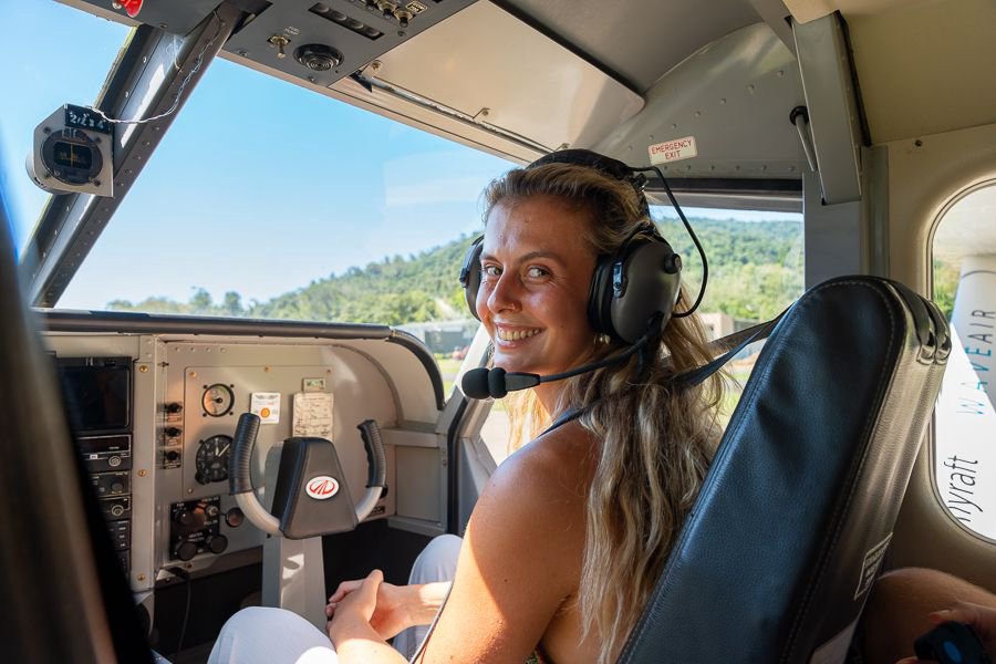 Smiling passenger wearing a headset seated inside a small scenic flight cockpit in the Whitsundays.