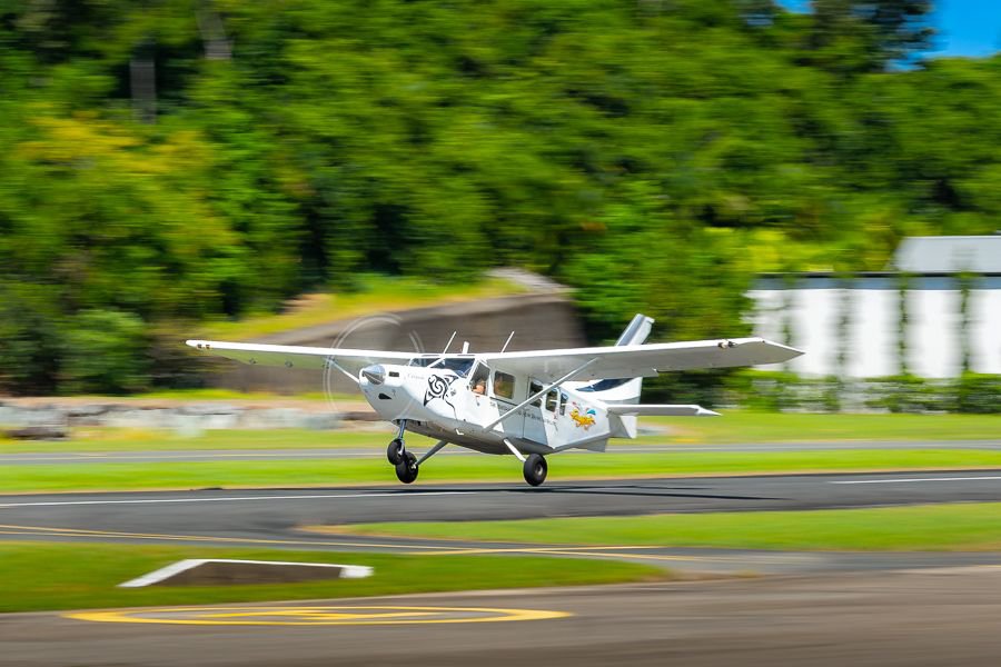 Small scenic airplane taking off from a tropical runway in the Whitsundays with lush green hills in the background.
