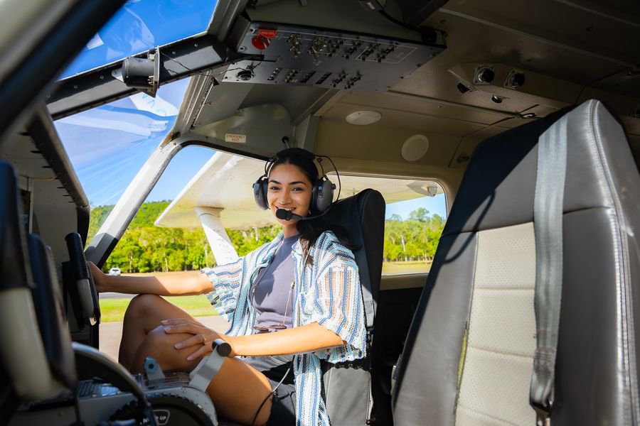 Young woman wearing a headset smiling from the front seat of a light aircraft before takeoff.
