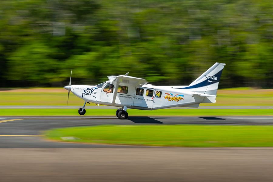 Light aircraft taking off from a tropical runway for a scenic flight over the Great Barrier Reef and Whitsundays islands.